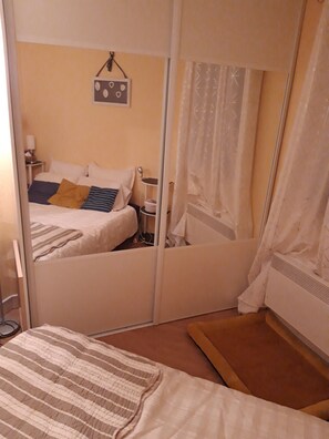 A bedroom with a bed, a bedside table, a mirror, and a curtain. - Near the beach, with an ocean view and a balcony (Saint-Cyprien)