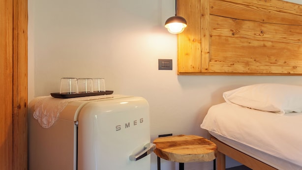 A bedroom with a bed, a wooden headboard, a small wooden stool, a white appliance with 'SMEG' on it, and a wall-mounted light fixture. - A Casa Da Angelo - Country House (Grottammare)