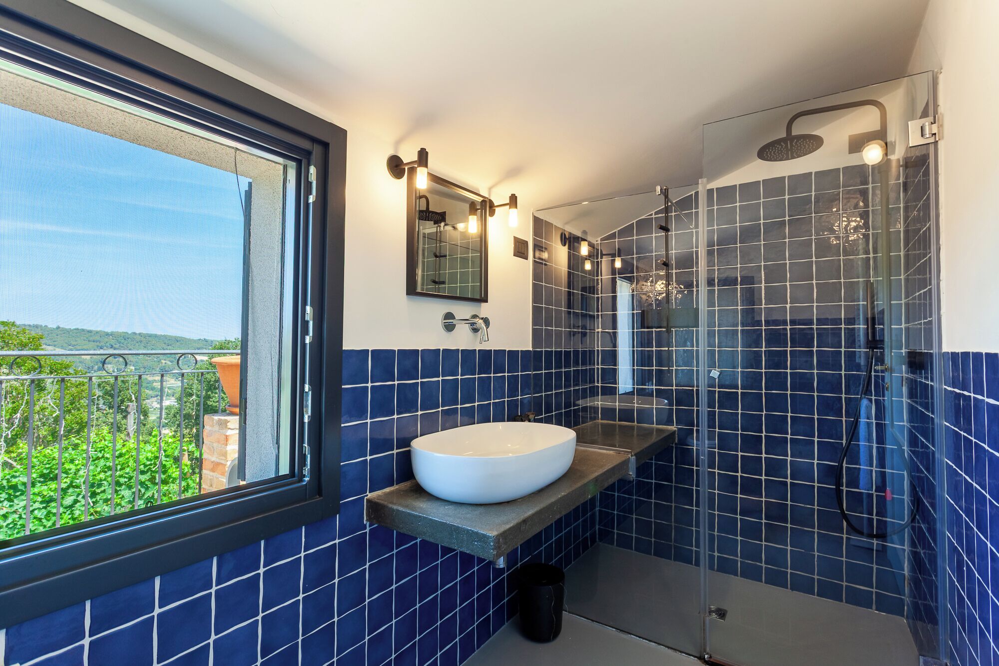 A bathroom with a large window, a white sink, and a glass-enclosed shower area.