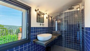 A bathroom with a large window, a white sink, and a glass-enclosed shower area.