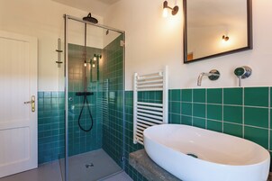Un baño con ducha de mampara de vidrio, un lavamanos blanco y paredes cubiertas de azulejos verdes.