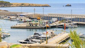 A marina with boats docked, a parking area, and a building with a blue and white color scheme. - Seafront Cala Ratjada Apartment (Cala Ratjada)