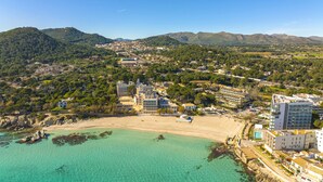 An aerial view of a coastal town with a beach, buildings, and mountains in the background. - Seafront Cala Ratjada Apartment (Cala Ratjada)