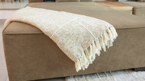 En beige soffa med en vit, strukturerad pläd.