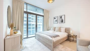 Una habitación de hotel moderna con una cama grande, una mesita auxiliar, una silla, un ventanal amplio y vistas a la ciudad.