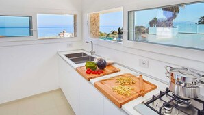Une cuisine moderne avec vue sur la mer, une cuisinière à gaz et une planche à découper avec des légumes.