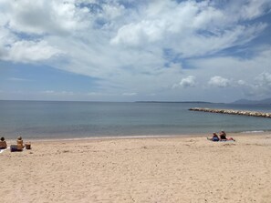 Ein Strand mit einem steinernen Wellenbrecher, ruhiger See und klarem Himmel.