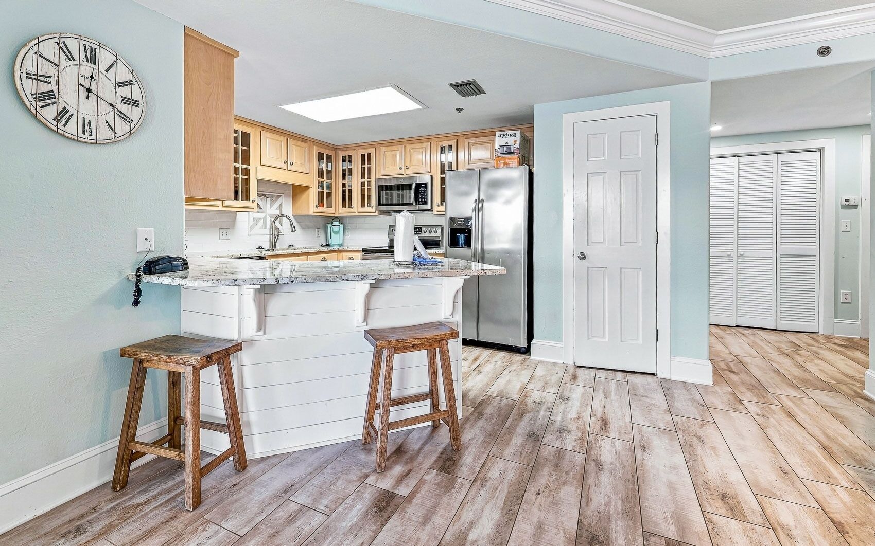 A kitchen with wooden cabinets, a stainless steel refrigerator, and a bar area with stools.