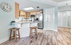 A kitchen with wooden cabinets, a stainless steel refrigerator, and a bar area with stools. - Phoenix VIII by Brett Robins Vacations (Orange Beach)