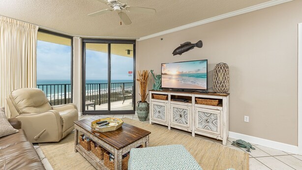 Ein Wohnzimmer mit einer Couch, einem Couchtisch, einem Fernseher, einem Schrank und Blick auf den Strand.