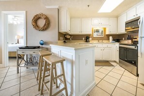 A kitchen with white cabinets, a central island, a built-in oven, and a dining area with stools. - Phoenix VIII by Brett Robins Vacations (Orange Beach)