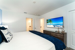 A bedroom with a bed, a dresser, a painting of a beach scene, and a door leading to another room. - 4312-Prologue (Kissimmee)