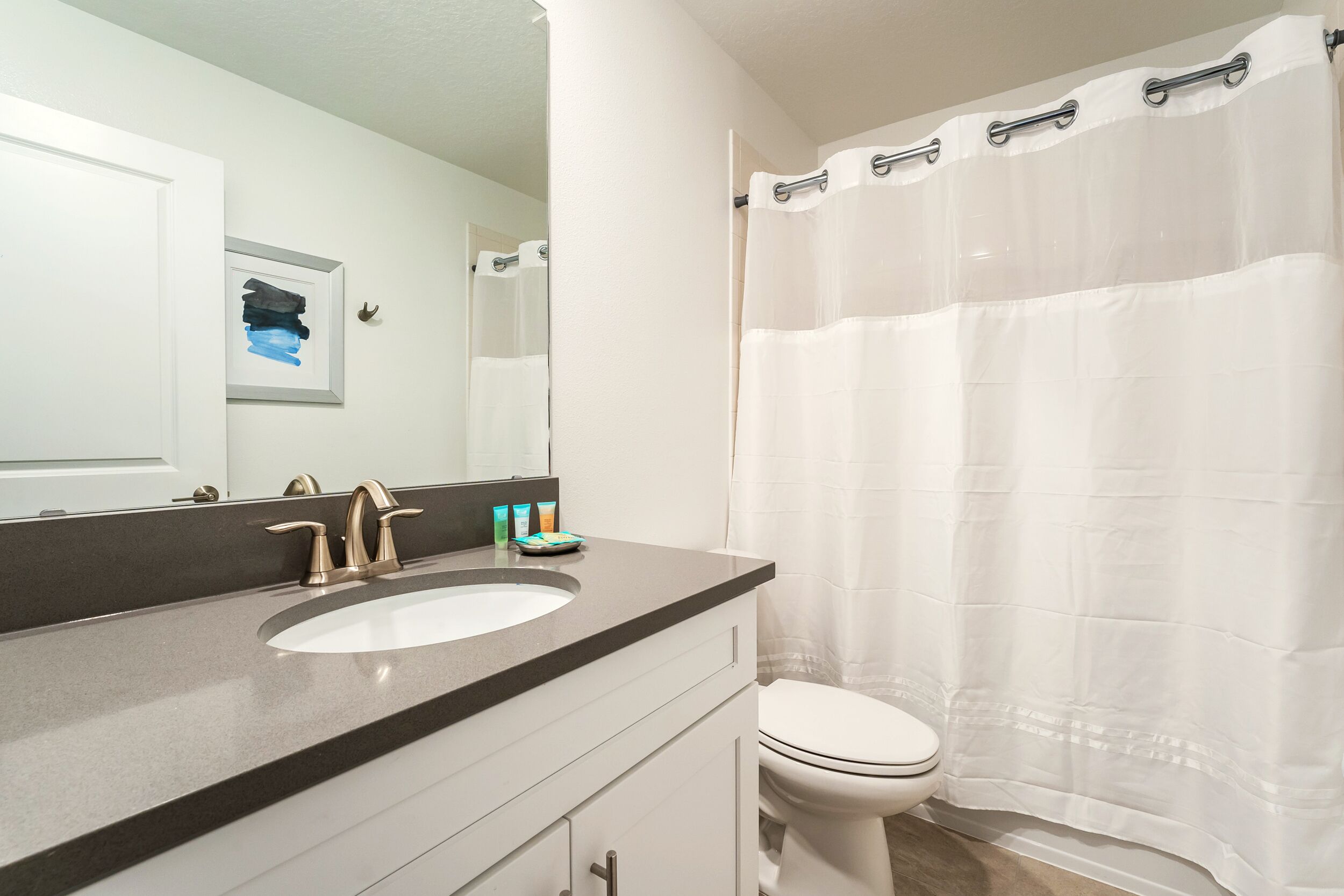 Een badkamer met een wit wastafel, een spiegel, een toilet en een douchegordijn.