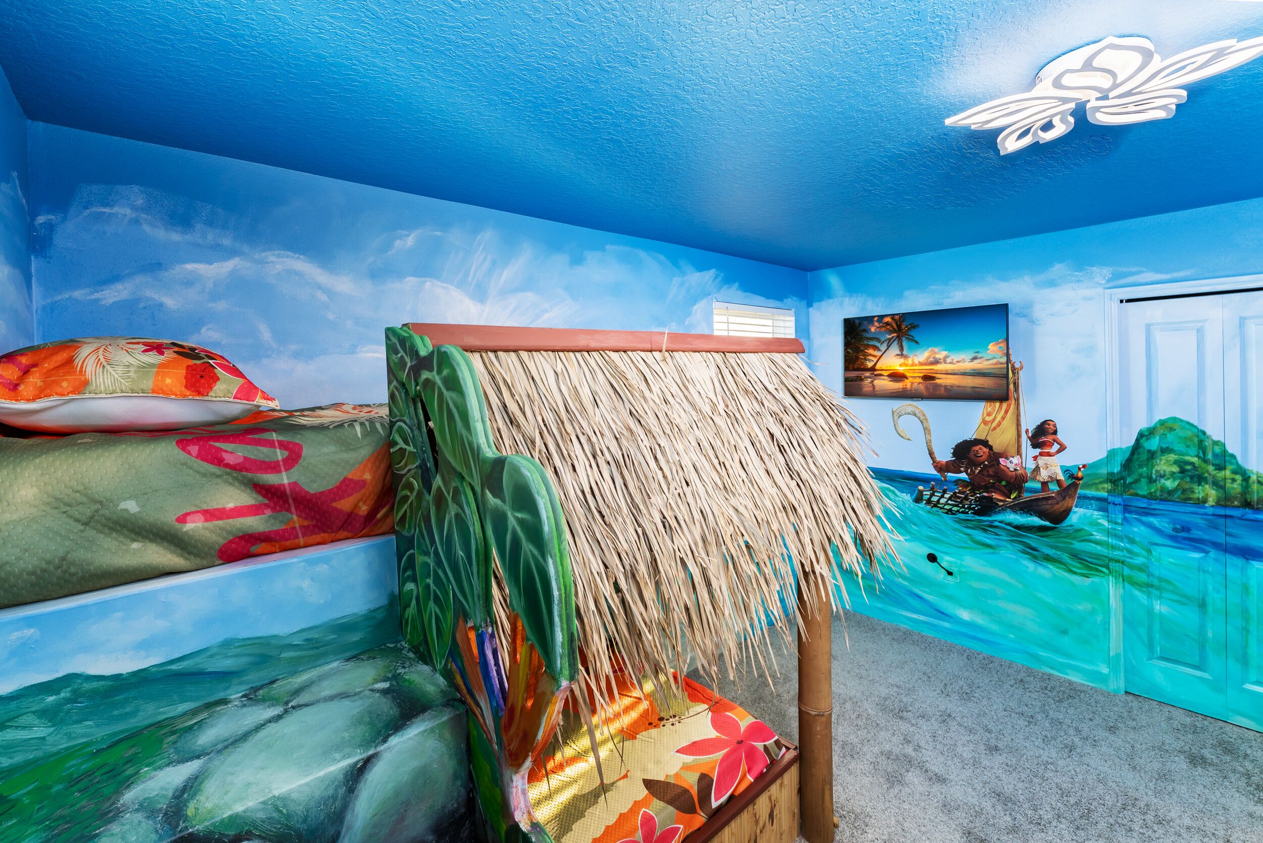 A room with a mural of a tropical beach scene, a bed with a thatched roof, and a painting of a sunset over water.
