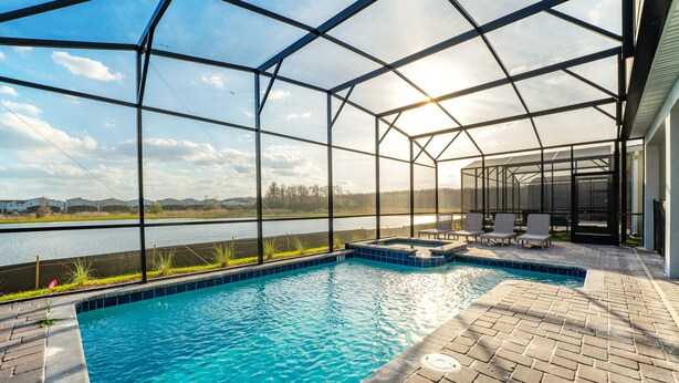 A swimming pool with a glass enclosure, a brick patio, and a view of a body of water and distant landscape. - 4312-Prologue (Kissimmee)