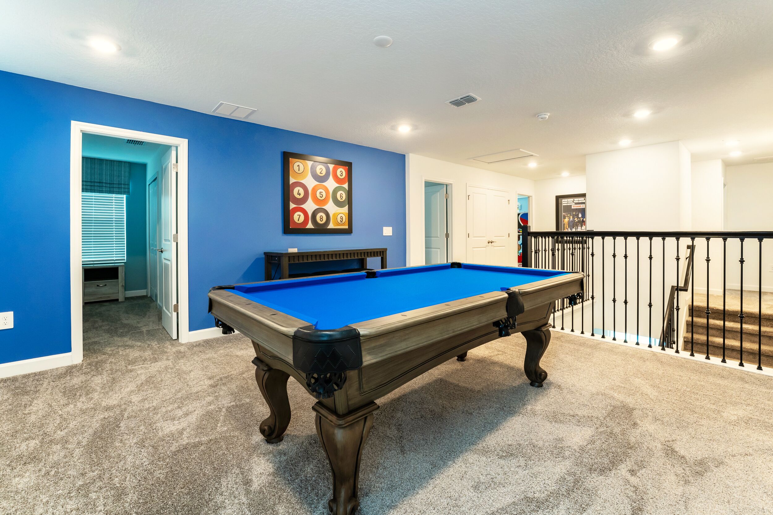 A pool table in a room with blue walls, carpeted floor, and a door leading to another room.