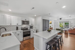 A modern kitchen with white cabinetry, stainless steel appliances, and a central island with stools.