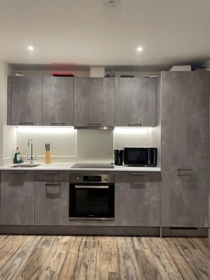 A modern kitchen with grey cabinets, stainless steel appliances, and a wooden floor. - Modern 1 bed Flat- 20mins From Central London (Romford)