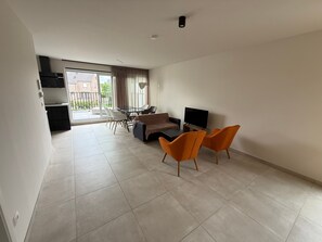 A modern living room with a sofa, two orange chairs, a TV, and a dining area with a table and chairs. - 4P 2B Casa Riemst Luxurious Entertainer s Dream (Riemst)