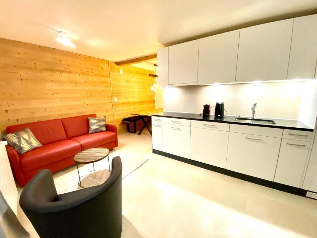 A modern kitchen with white cabinets and a red sofa in the living area.