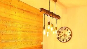 A wooden dining table with benches, a wall-mounted clock, and hanging pendant lights.