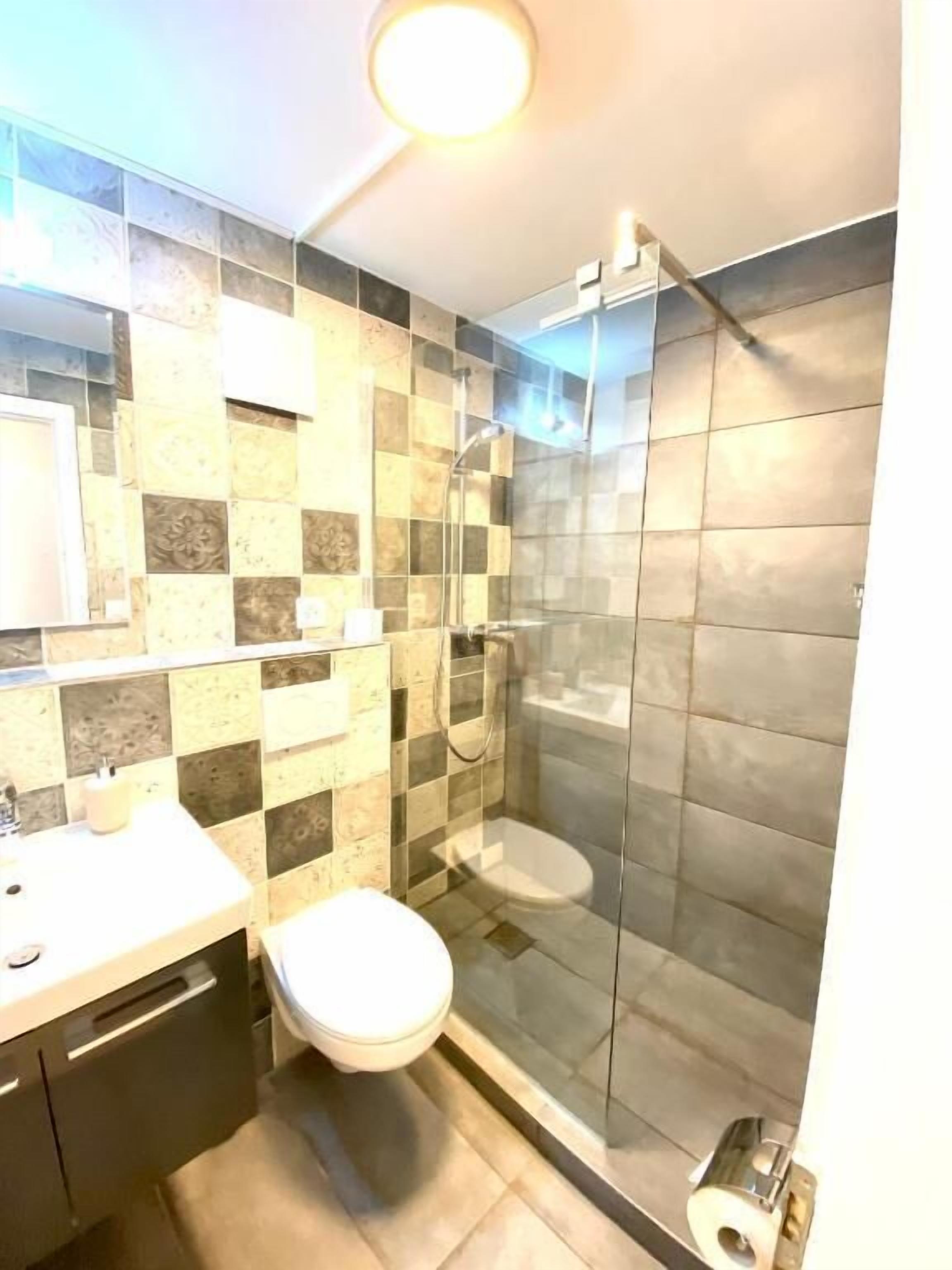 A bathroom with a glass shower enclosure, a toilet, and a sink with a mirror.