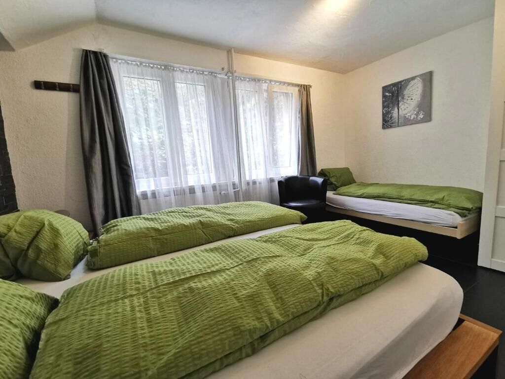 A room with two beds, a chair, a window with curtains, and a wall-mounted picture.