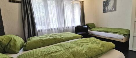 A room with two beds, a chair, a window with curtains, and a wall-mounted picture.
