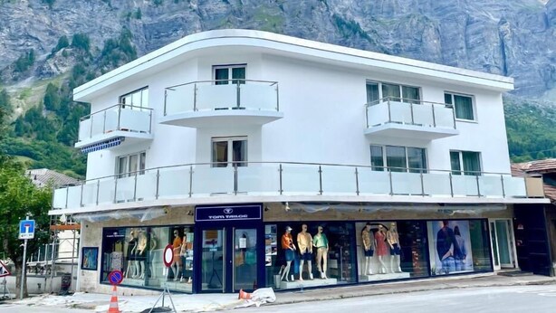 A white building with a storefront featuring mannequins, set against a mountainous backdrop.