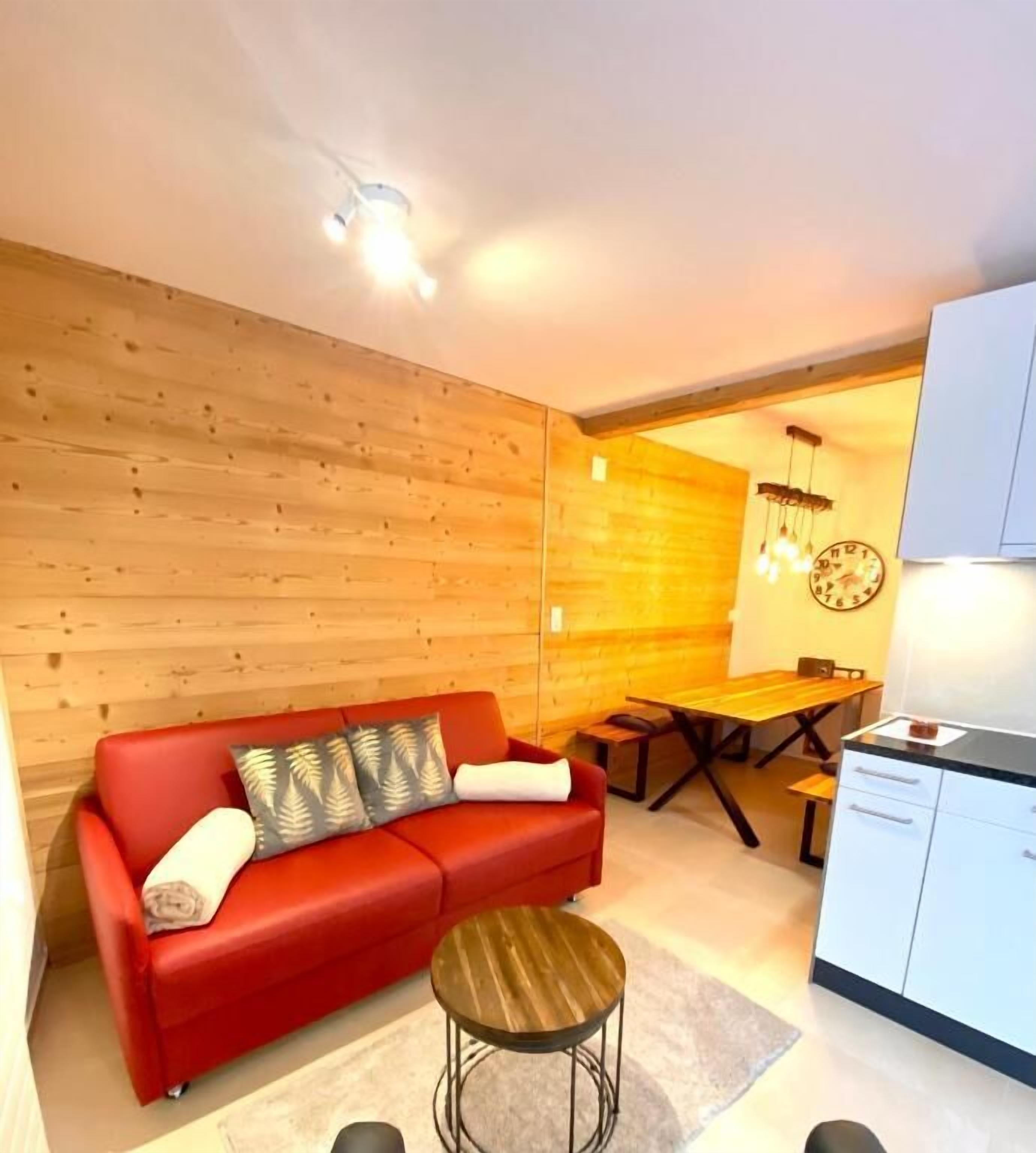 Een moderne woonkamer met een rode bank, houten wanden, een eettafel en een keukenhoek.