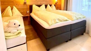 A hotel room with a wooden wall, two beds, a bedside table with a lamp, and a window with curtains.