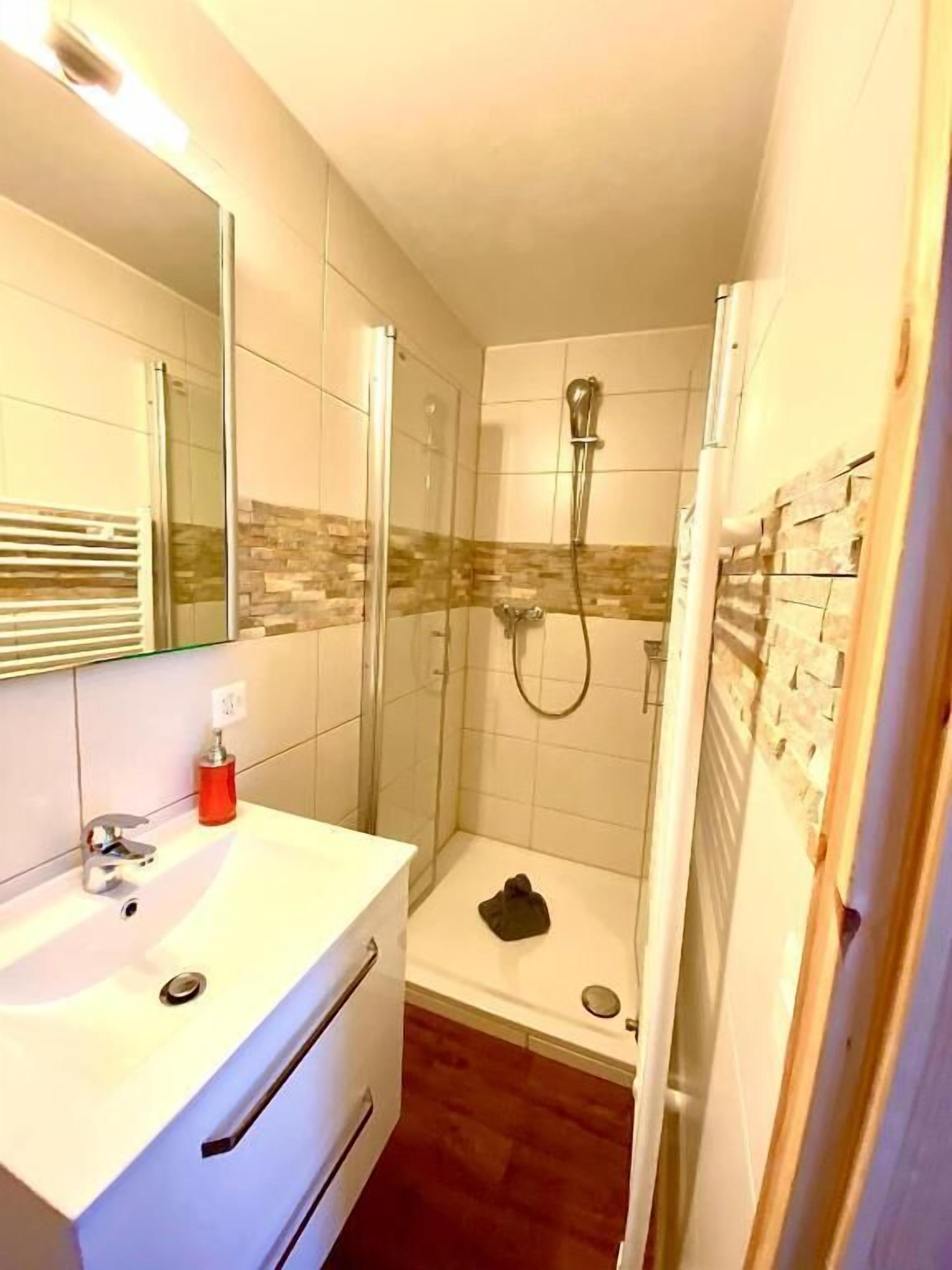 A bathroom with a glass shower enclosure, a white sink, and a tiled shower area.