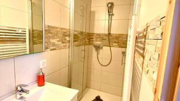 A bathroom with a glass shower enclosure, a white sink, and a tiled shower area.