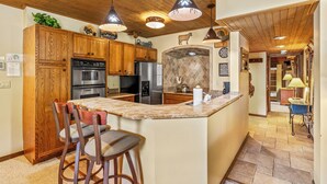 A kitchen with wooden cabinets, a central island, bar stools, and pendant lighting. - Slope-Side Retreat at the Steamboat Resort Base Area (Steamboat Springs)