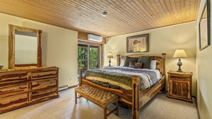 A bedroom with a wooden ceiling, a bed with a quilt, a wooden bench, a dresser, and a nightstand with lamps. - Slope-Side Retreat at the Steamboat Resort Base Area (Steamboat Springs)