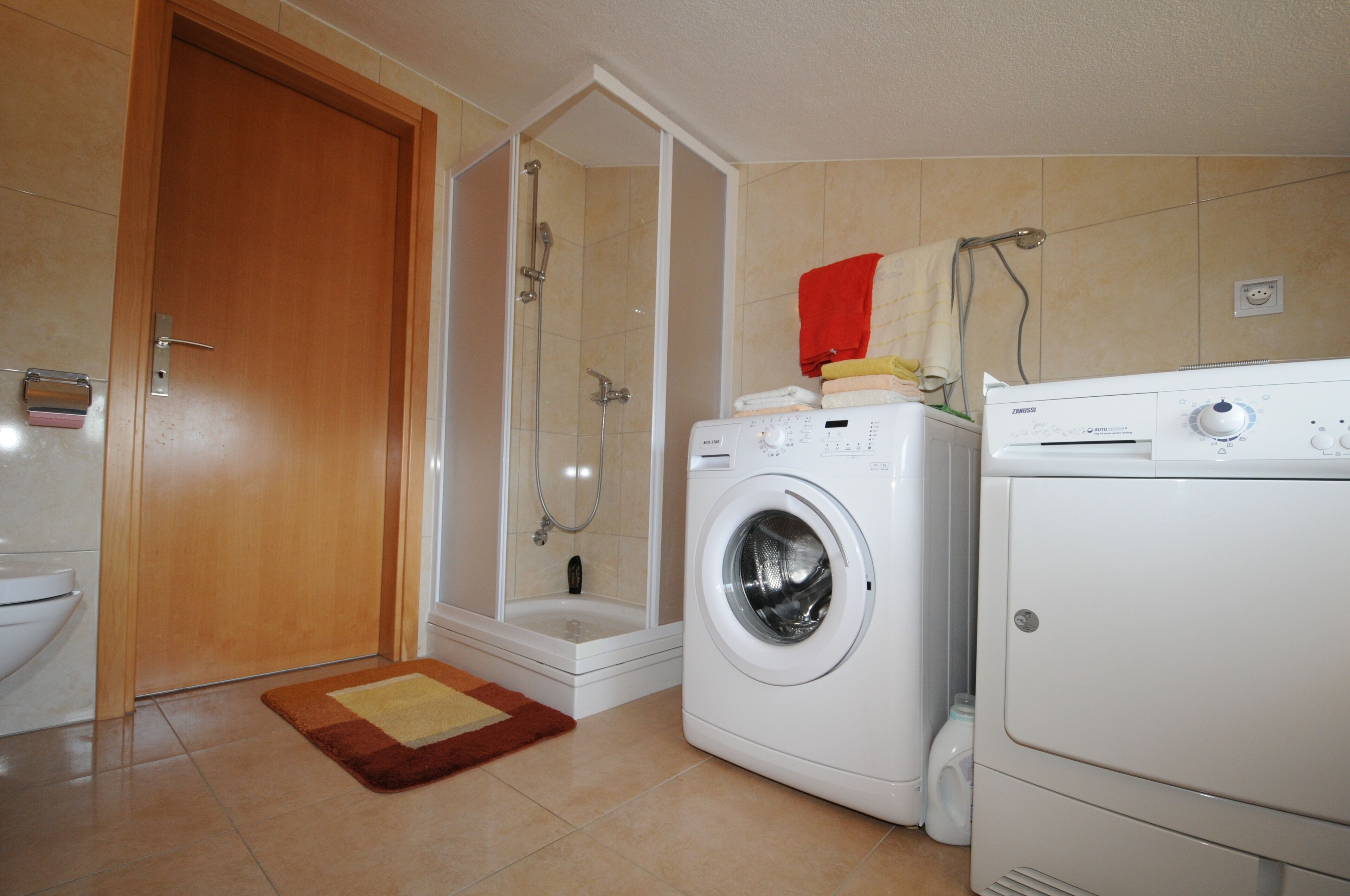 Een badkamer met een douche, toilet, wasmachine en handdoekrek.