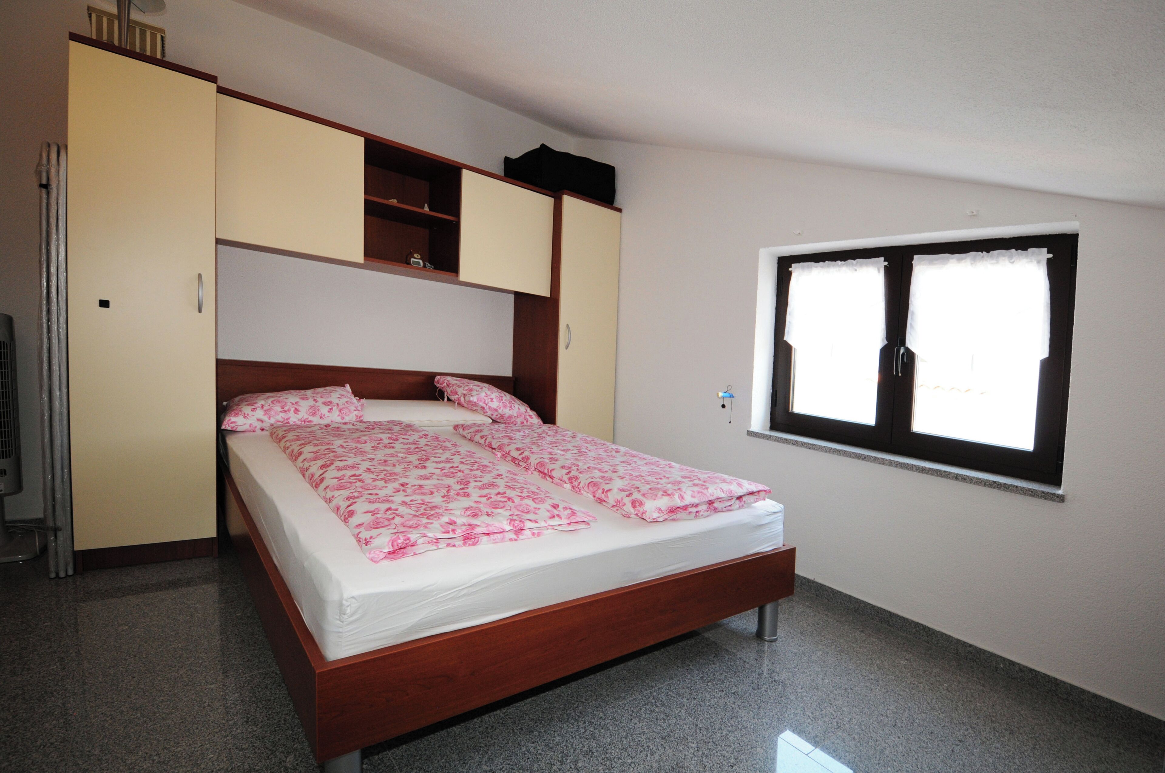 Ein Schlafzimmer mit Bett, Schrank, Fenster und Heizkörper.