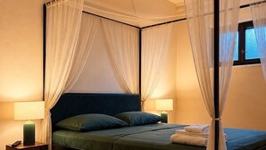 Een bed met baldakijn voorzien van dunne gordijnen, een nachtkastje met lamp, en een raam met uitzicht.