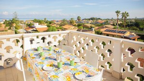 Un balcon avec une table dressée pour le dîner, donnant sur un quartier résidentiel avec des maisons et des palmiers.