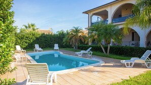 Une piscine avec des chaises longues, un bâtiment doté de balcons et des palmiers.
