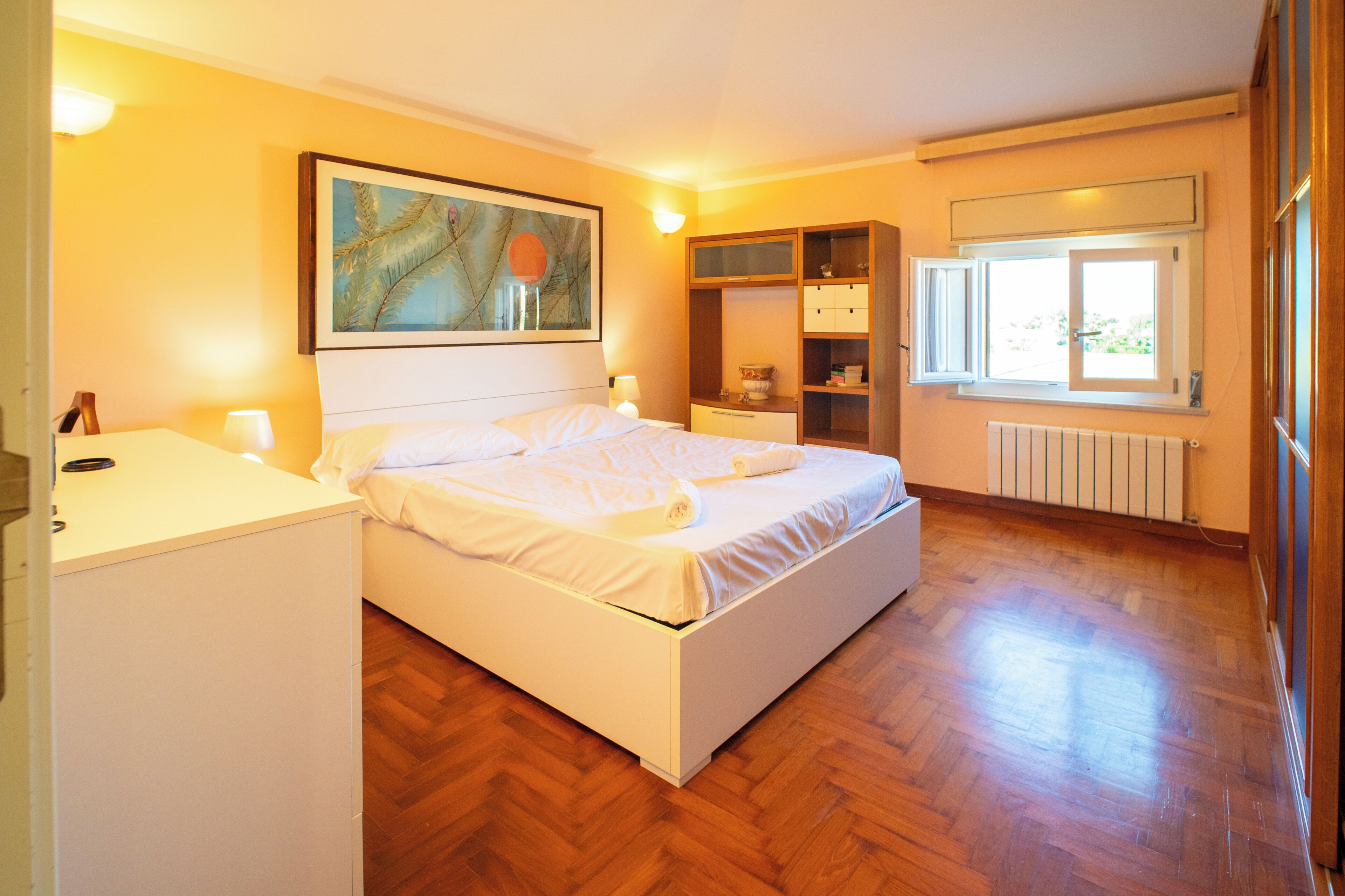 Un dormitorio con cama, mesitas de noche, armario, radiador y ventana.