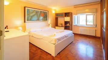 Un dormitorio con cama, mesitas de noche, armario, radiador y ventana.