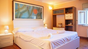 Un lit bien fait, avec du linge de lit blanc, une table de chevet avec une lampe, un grand tableau au mur et une armoire intégrée avec des étagères.
