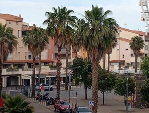 Eine Straße mit Palmen, parkenden Autos und Gebäuden, an denen Schilder wie 'FRUIT HOUSE' und 'ANISIA' erkennbar sind.