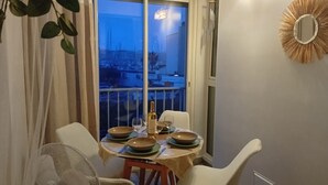 En matplats med ett bord dukat för två personer, ett fönster med utsikt över byggnader och en dekorativ spegel på väggen.