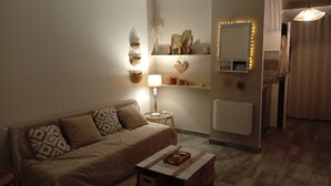 Ett mysigt vardagsrum med en soffa, ett litet sidobord, en lampa, en spegel med belysning och ett element.