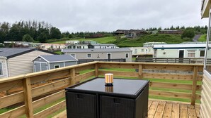 A wooden deck with a table and chairs, overlooking a row of mobile homes. - Sleeps4-familyfriendly-greatamenities-freeparking (Newton Stewart)