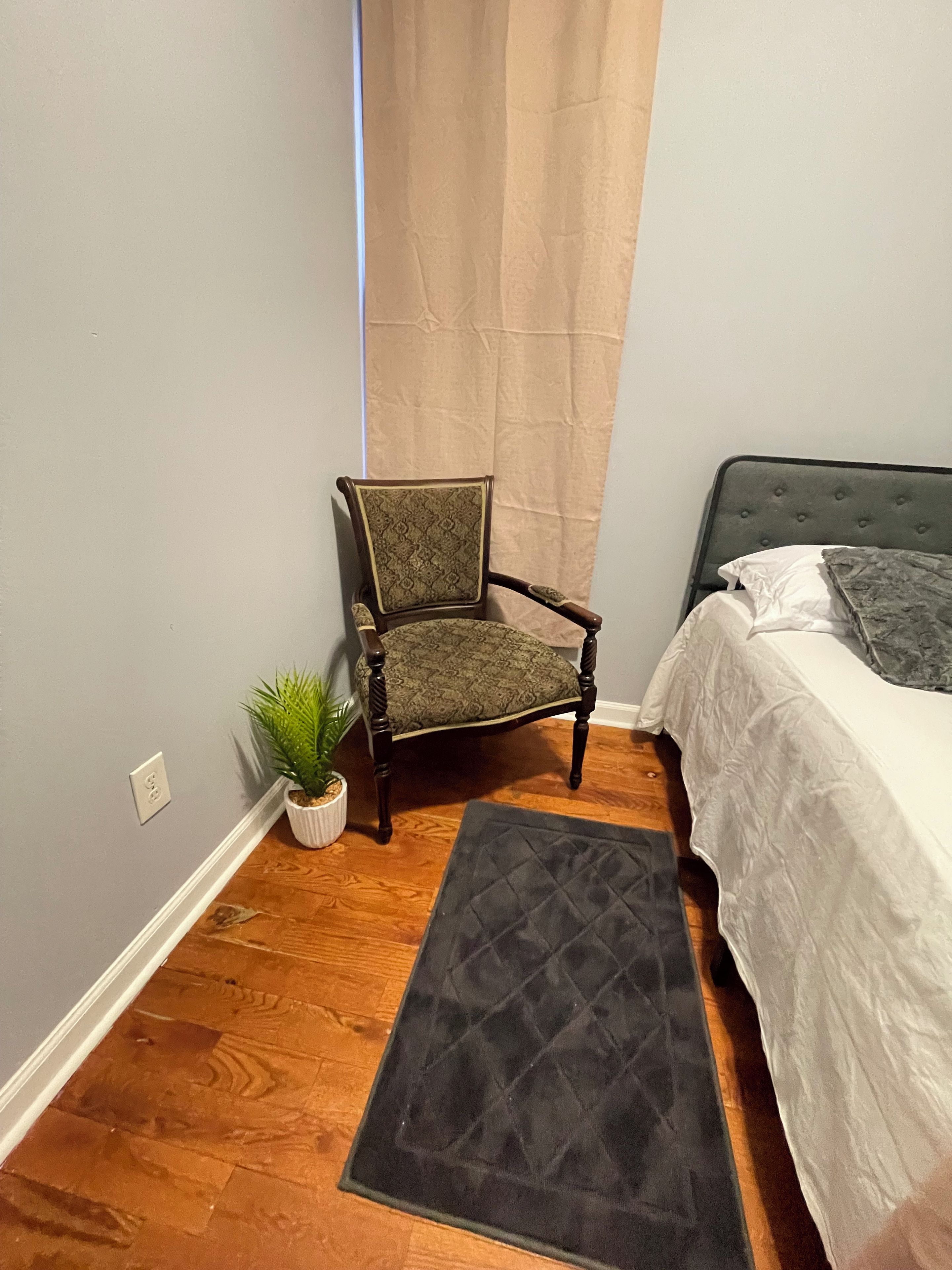 Une chambre à coucher avec un lit, une chaise, un tapis et une plante en pot.