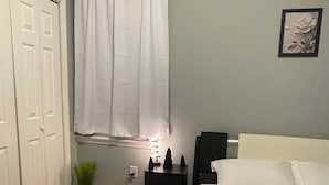 Et soveværelse med seng, et natbord, en potteplante, et vindue med gardiner og en dør.