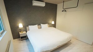 Quarto de hotel com uma cama grande, duas luminárias de cabeceira, uma mesa de apoio, ar condicionado fixado na parede e uma porta.